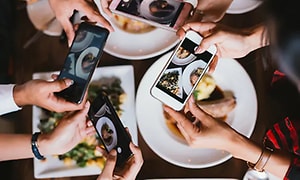 Fyra personer fotograferar en maträtt med sina mobiltelefoner.