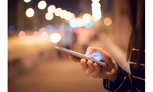 Någon håller i en mobiltelefon med stadsljus i bakgrunden.