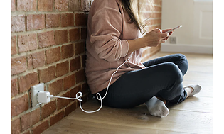 En kvinna sitter på golvet och laddar sin smartphone.