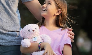 En liten flicka håller i ett gosedjur med en (bluetooth /GPS) tracker.
