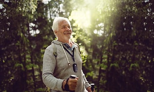 En äldre man med gåstavar promenerar ute i skogen.
