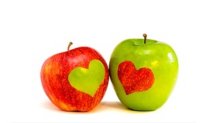 Ett grönt och ett rött äpple med utkarvade hjärtan i.