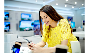 En lycklig kvinna står med en mobiltelefon i en elektronik butik.
