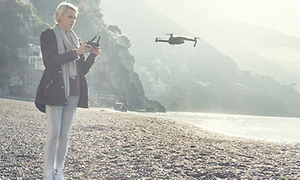 Kvinna flyger en frönare på en strand. Drönare befinner sig ca en meter framför henne och hon har en kontroll i handen.