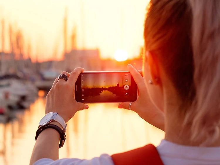 En kvinna tar ett foto av en solnedgång i en hamn.