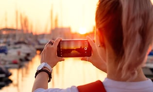 En kvinna tar ett foto av en solnedgång i en hamn.