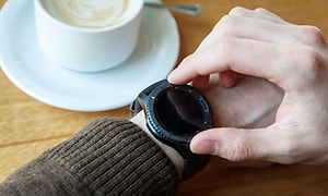 En person kontrollerar sin smartwatch medan han dricker kaffe.