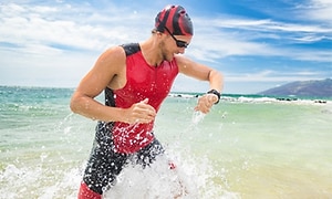 En man i simkläder kommer upp från vattnet och kollar på sin smartwatch.