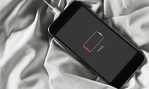 Iphone placerad på ett mjukt underlag och inkopplad till eluttag, symbolen på displayen visar att den laddar.