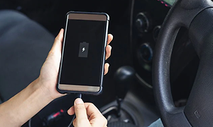 En person som sitter på förarsätet i bilen kopplar in sin telefon på laddning då batteriet nästan är helt slut.