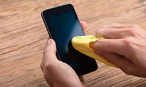 Närbild på händer som torkar av skärmen på en mobiltelefon med en gul trasa.