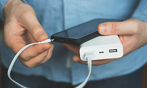 Man ansluter en vit powerbank till en svart mobiltelefon med en vit kabel.