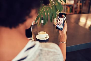 Kvinna i videosamtal med en man på cafe, troligen Facetime. En kopp kaffe på ett bord syns i bakgrunden. 