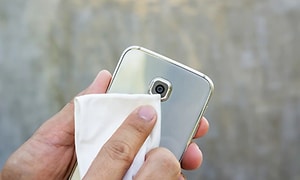 En person rengör linsen på en mobilkamera med en vit trasa. 