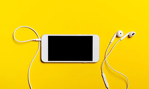 En vit iphone placerad på illgul bakgrund med vita earphones anslutna till telefonen.