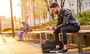 Två män som sitter på parkbänkar långt ifrån varandra och ser på sina mobiltelefoner. 