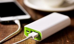 En vit iphone ligger på ett bord och är kopplad till en vit powerbank med gröna detaljer för att ladda upp batteriet. 
