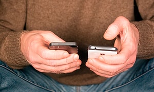 Man håller två olika mobiltelefoner i händerna, en iphone och en android, en vit och en svart. 
