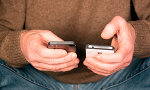Man håller två olika mobiltelefoner i händerna, en iphone och en android, en vit och en svart.