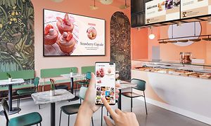 Samsung Business TV-app visas på en telefon med skärm bakom.