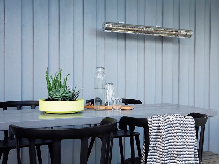 Terassvärmare upphängd på en grå vägg ovanför en matbord utomhus