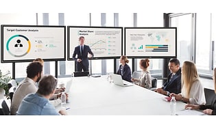 En man har en presentation på 3 skärmar på ett möte.