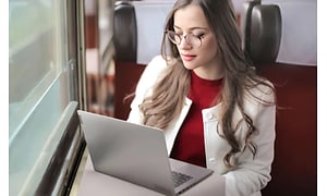 Kvinna sitter med en Lonovo Thinkbook framför sig på tåget, vid en fönsterplats med bord. 