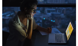 Kvinna i mörkt rum sitter framför en Lonovo Thinkbook med skärm som lyser upp och tangenter med bakgrundsljus.