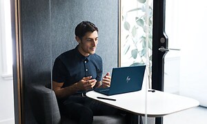 Man som sitter vid ett bord med en bärbar HP-dator uppställd framför sig i ett mindra mötesrum. 