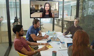 Här sitter fyra personer i möte på ett mötesrum tillsammans med en tjej som är uppkopplad på videokonferens. 