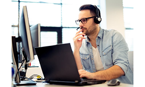 En man med headset och mikrofon sitter vid ett skrivbord med flera datorskärmar framför sig.