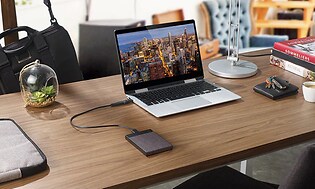 En laptop placerad på ett skrivbord med en extern hårddisk inkopplad. Bredvid ligger en hög ed böcker, en plånbok, bilnyck