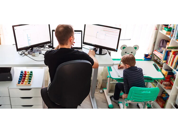 Man som sitter hemma vid ett skrivbord och arbetar, med ett mindre skrivbord bredvid där en pojke sitter och tecknar. 