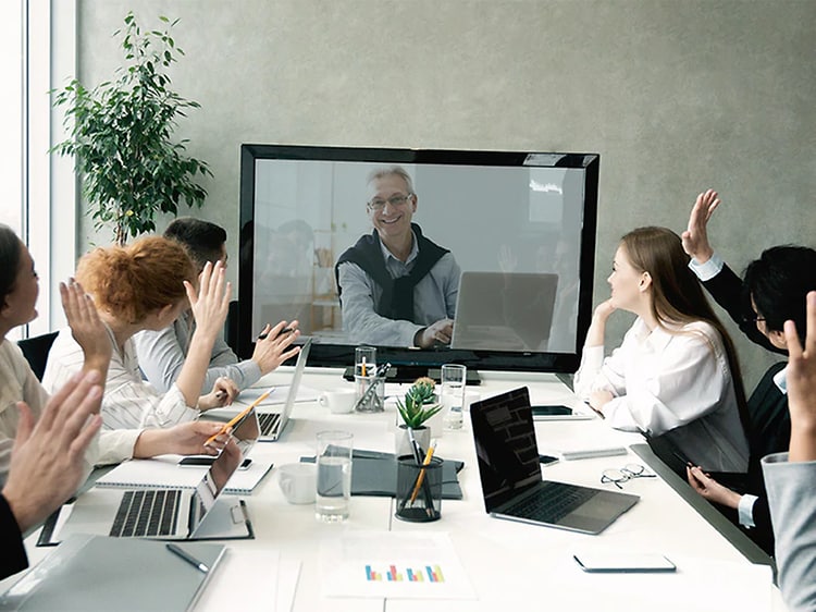 Mötesrum fullt med folk som alla tittar på en skärm där en till deltagare är ansluten via en så kallad videokonferens.