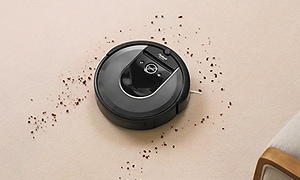 En rund svart robotdammsugare av märket iRobot Roomba i7+ suger upp skräp på golvet. 