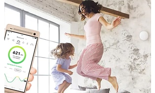 En liten dosa som ser ut som en mobiltelefon talar om vilken nivå luftfuktigheten är på. En kvinna och ett barn hoppar i sängen.