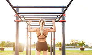 Kvinna i svarta shorts och sport bh tränar pull-ups i utegym med sportklocka på. 